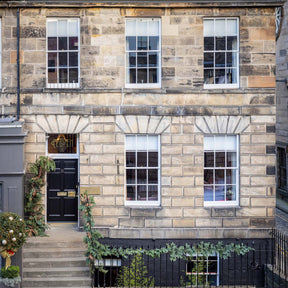 Two-story stone building with white windows and a black door on a street.